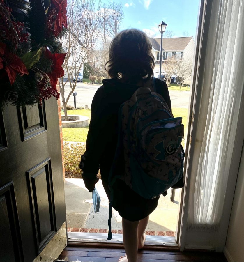 Student carrying a backpack and holding a mask, walking out the door to go to school.